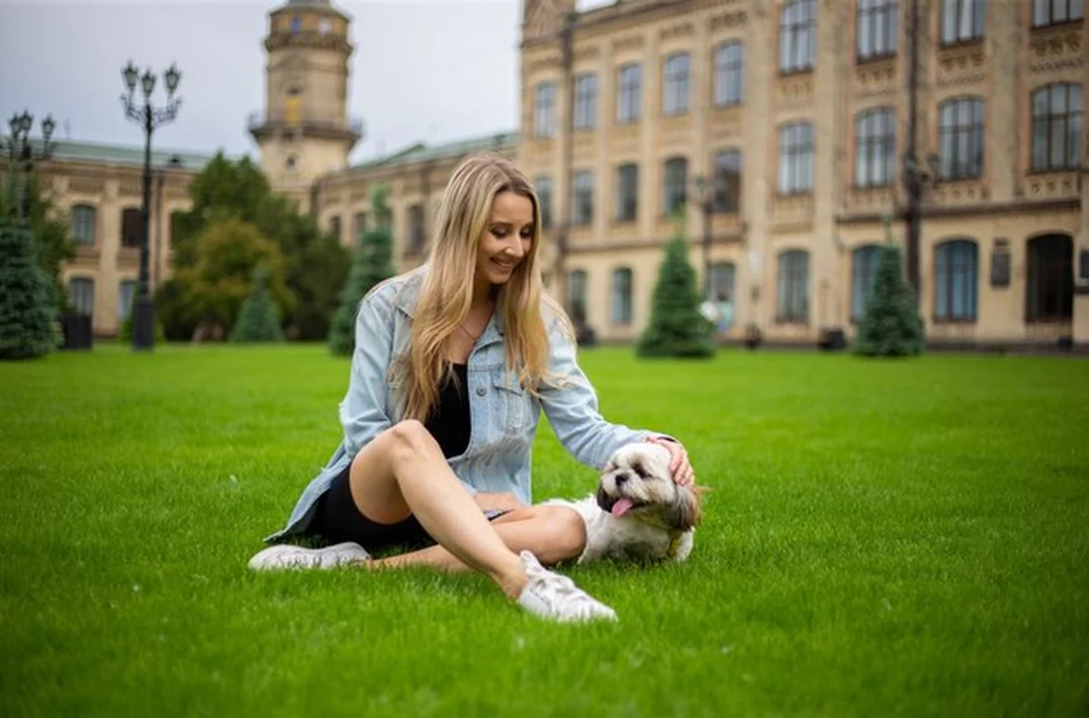 Młoda kobieta w dżinsowej kurtce bawi się z psem na trawie obok stadionu